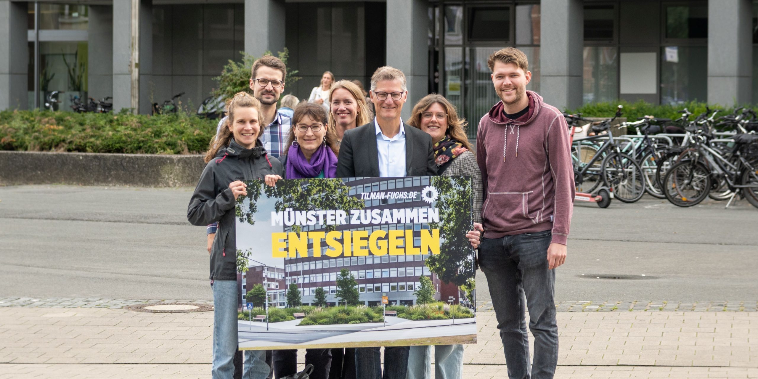 Die Grünen Kandidat*innen mit einem KI-Foto der Entsiegelung vor dem Stadthaus 2